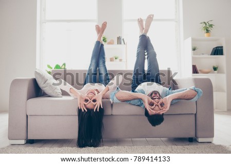 We go crazy and have fun together! Beautiful cheerful delightful humorous couple of two lovers clothed in casual denim outwear, demonstrating binoculars using hands, lying upside-down 商業照片 © 