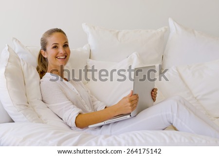 Young woman in a white atmosphere, surfing the net lying on a sofa at home.