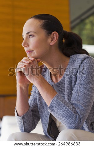Woman in grey cardigan thinking with fingers crossed under her chin.