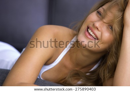 Smiling young blond woman lying down on blue sofa.