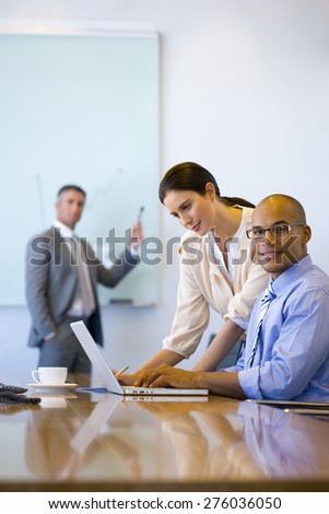 Male and female executives working together in a meeting room with trainer using white board in the background.