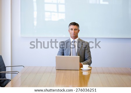 Business manager sitting at the end of a meeting table, with cup of cafe and laptop.
