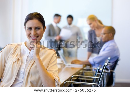 Portrait of female executive in a meeting room with coworkers in the background.