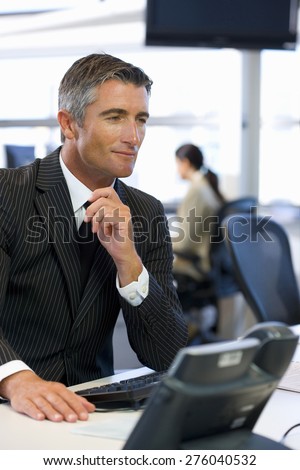 Business executive dressed in black, sitting in front of a computer in open space office.