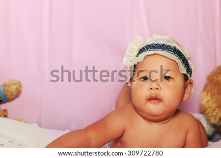 The little baby girl with blue hair band lying prone on the bed pink.