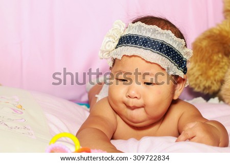The little baby girl with blue hair band lying prone on the bed pink.