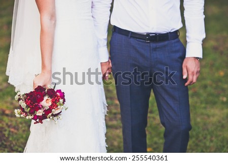 Bride hold groom by the hand and wedding bouquet. Focus on wedding flower bouquet. Crop by chest and legs. Bride in wedding dress, groom wears classic clothes. Vintage style coloring