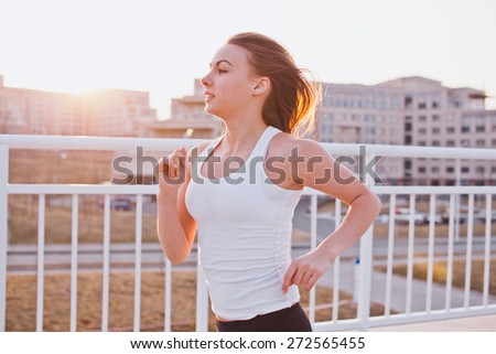 Attractive young woman in sports shirt running outdoors in evening. Loose hair. Sunset on background. Half-length portrait. Vintage coloring