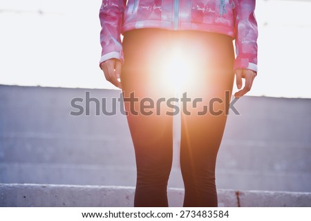 Girl standing at sunset with sun between her legs on a stadium stand. Yoga, femininity and yin concept. Vintage coloring