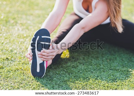 Girl stretching her foot on a grass on stadium field. Warming up before training. No face