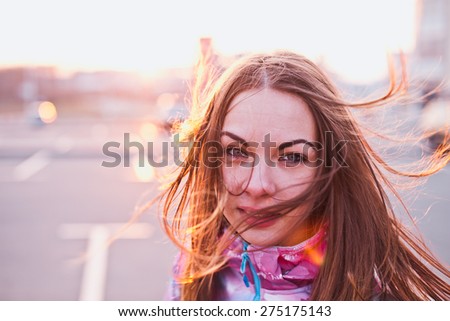 Attractive girl with wind fluttered hair looking in a camera on a parking lot at a sunset. Traveling, life and freedom concept. Copy space