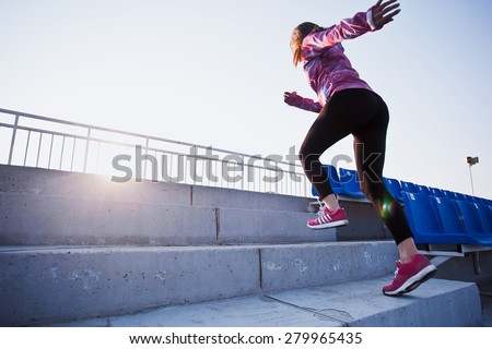 Girl runs upstairs to a sunset. Young woman in sportswear training on a stadium. Copy space. Healthy lifestyle in a city concept