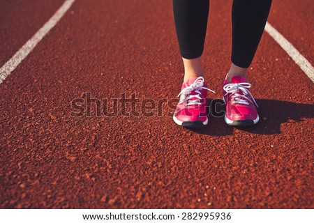 Close-up of feet and calf of young sporty woman on a red race track. Front view. Copy space