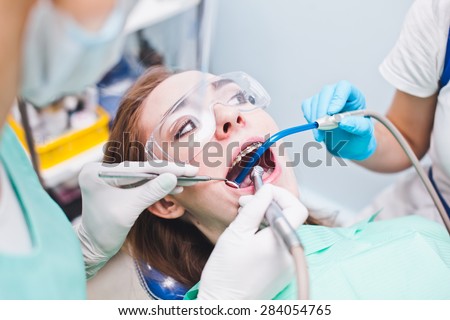 Woman patient with dental braces in dentist chair looking at a dentist assistant during procedure. Dentist in a mask examining her client in dentist office
