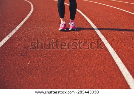 Sporty woman feet on a race track front view. Preparing for run. Brightly lit scene. Copy space