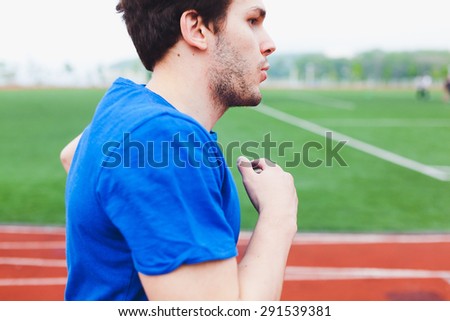 Man runner in blue shirt running hard with tense with stadium field and race track background. Dynamic photo of young athlete