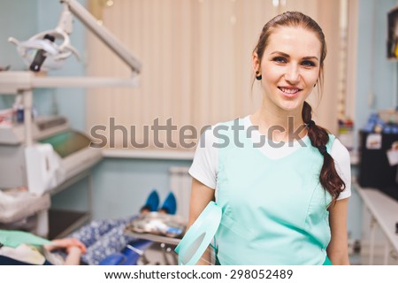 Young beautiful woman dentist smile cheerfully when holding full face protection shield standing in her office in front of dental chair with patient. Copy space