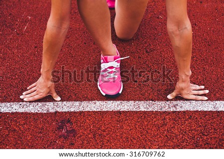 Young fit woman runner athlete at start position in steady pose close to white starting line on stadium with muscled stressed hands and leg at the line preparing to run. Unrecognizable no face photo