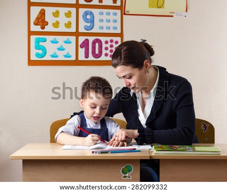 teacher teaches a young child at a school desk