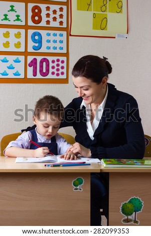 teacher teaches a young child at a school desk