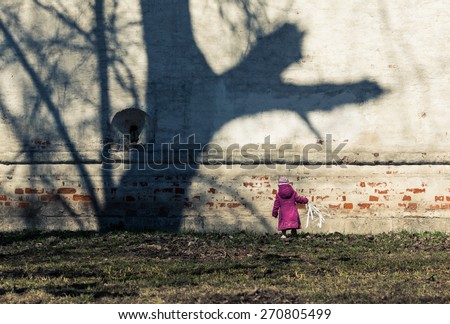 Adorable little girl in pink coat staying near the wall. Unusual tree shadows contrasts with little girl. Color and size contrast.