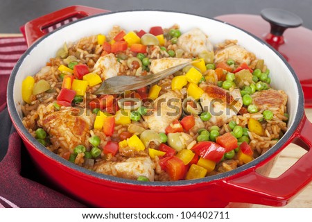 Chicken and rice dish, arroz con pollo, from Latin America, with chicken, rice, beer, tomatoes, capsicums, peas, paprika, cumin, oregano, in a red cast iron casserole.