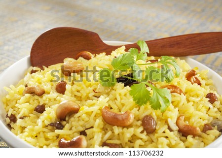 Classic fruit and nut Indian pilau, basmati rice cooked with stock, saffron, garlic, onion, cinnamon, cardamom, sultanas and garnished with cashew nuts and coriander. Focus on centre.