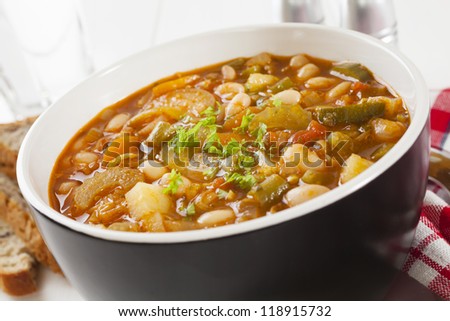 A bowl of vegetable soup on a table with bread.