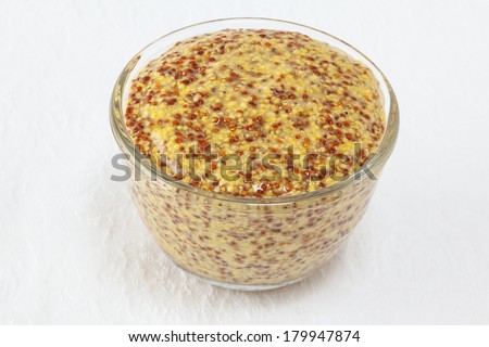 Wholegrain mustard in a small glass dish on a white textured cloth background.