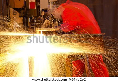 Blurred welder busy in workshop manufacturing metal construction. Many sparks shower from the torch.