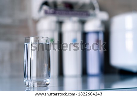 Pure water in glass and water filters on the blurred background. Household filtration system.