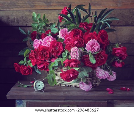 Red and pink roses in a basket against from boards. A still life with a bouquet of roses in a basket and hours on a wooden table.