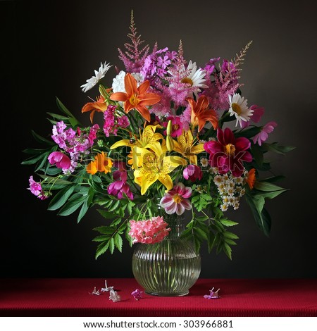 Bouquet from cultivated flowers in a jug on a red cloth