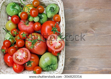 Fresh red and green tomatoes in a basket on a table at the left, on the right a blank space for the text, the top view. Tomatoes mature and immature. The cut tomato.