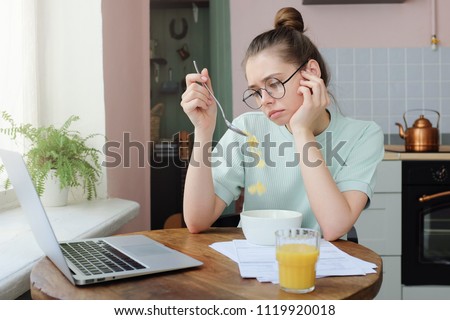 Young woman with no appetite, tired, bad mood and sleepy, sitting in the pastel kitchen, having unsavory unpalatable unappetizing breakfast Stock foto © 