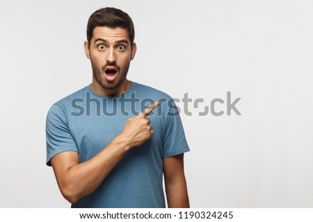 Young surprised man in blue t-shirt pointing right with his finger, shouting WOW, isolated on gray background with copy space fot your text. Shock content Stockfoto © 