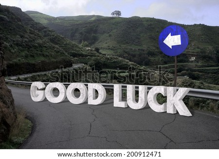 concept image showing a old remote road bending through the landscape with good luck text on it in white stone letters and traffic sign