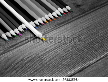 Black and white image of colored pencils with isolated pencil against a dark wooden table. The concept of personality, distinctive character