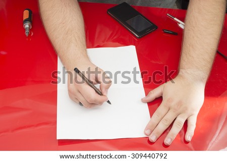 A man writing on a piece of paper on a cluttered desk.
