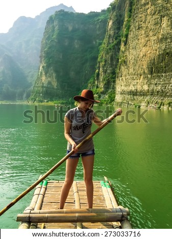 Pretty girl floating on a bamboo raft on the green water of lake, Shidu, China. Shidu conservation area is one of the most beautiful places with unique nature in China.