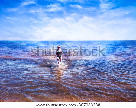 Beautiful young woman walking between shining water of blue sea. She feels freedom and happiness walking in splashes of water. There are only she, water and sky.