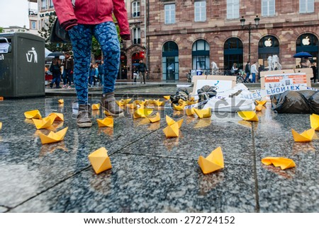 STRASBOURG, FRANCE - APR 26 2015: Woman walking over yellow paper boats at protest against immigration policy and border management which asks for commitment in the wake of migrants boat disasters