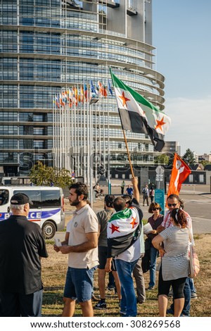 STRASBOURG, FRANCE - AUG 20, 2015: People protesting in front of European Parliament denouncing the Syrian airstrikes on Douma wheremore 80 were killed - waving flag of Syria European Parliament