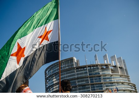 STRASBOURG, FRANCE - AUG 20, 2015: People protesting in front of European Parliament denouncing the Syrian airstrikes on Douma  - flag of Syria with Parliament building in the background