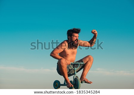 Guy riding childs tricycle. Portrait of a bearded man as a crazy hipster having fun with bicycle outdoors. Excited young male riding a small bicycle and gesturing happiness