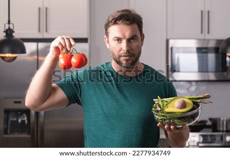 Taking care of health. Handsome man in casual t-shirt standing in the kitchen at home. Young man cooking vegetables in the kitchen. Dieting man with bowl of salad. Green salad healthy food concept. Photo stock © 