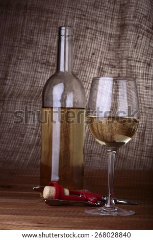 Wine bottle, opener and glass with white wine standing on burlap background