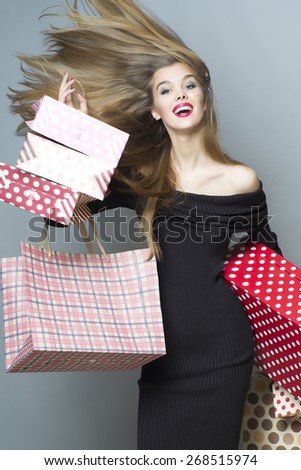 Stylish shopping girl with streamed hair in the breeze looking forward holding colorful packages and box, vertical picture