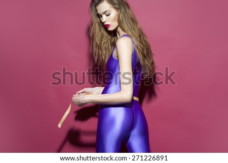 Stylish slim girl in violet second skin jumpsuit standing on her back with tape-line around torso on purple background copyspace, horizontal picture
