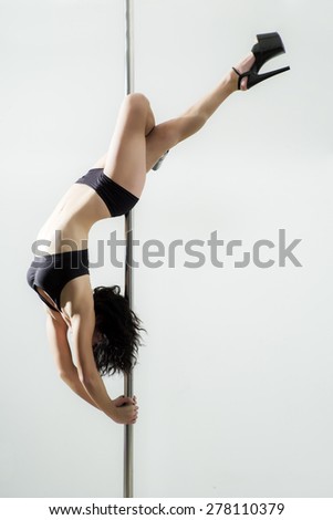 Flexible sexy woman dancing in black lingerie on the pole on white background copyspace, vertical picture
